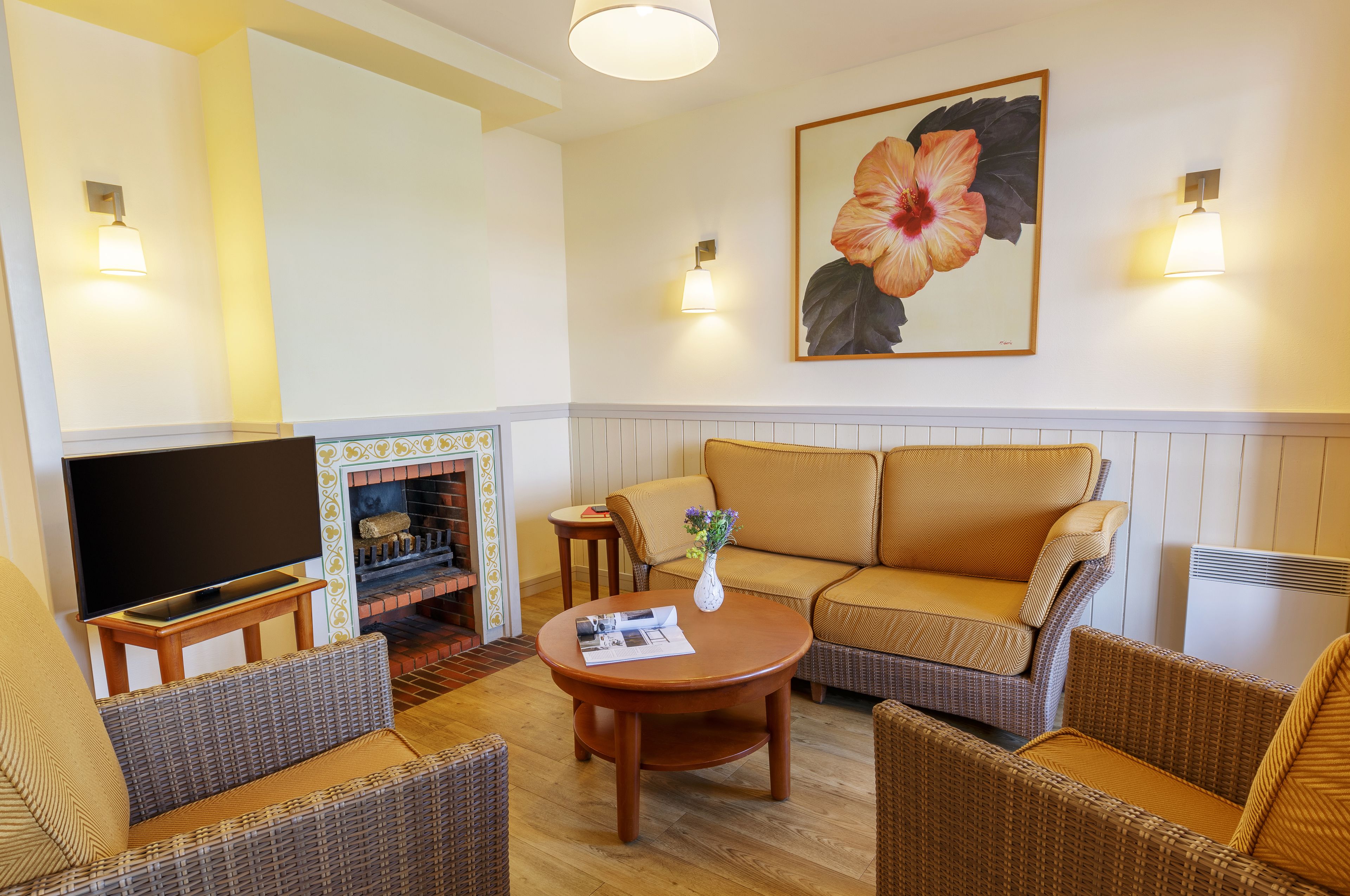 A living room with a sofa, two armchairs, a coffee table, a flat-screen TV, a fireplace, and wall-mounted lamps.