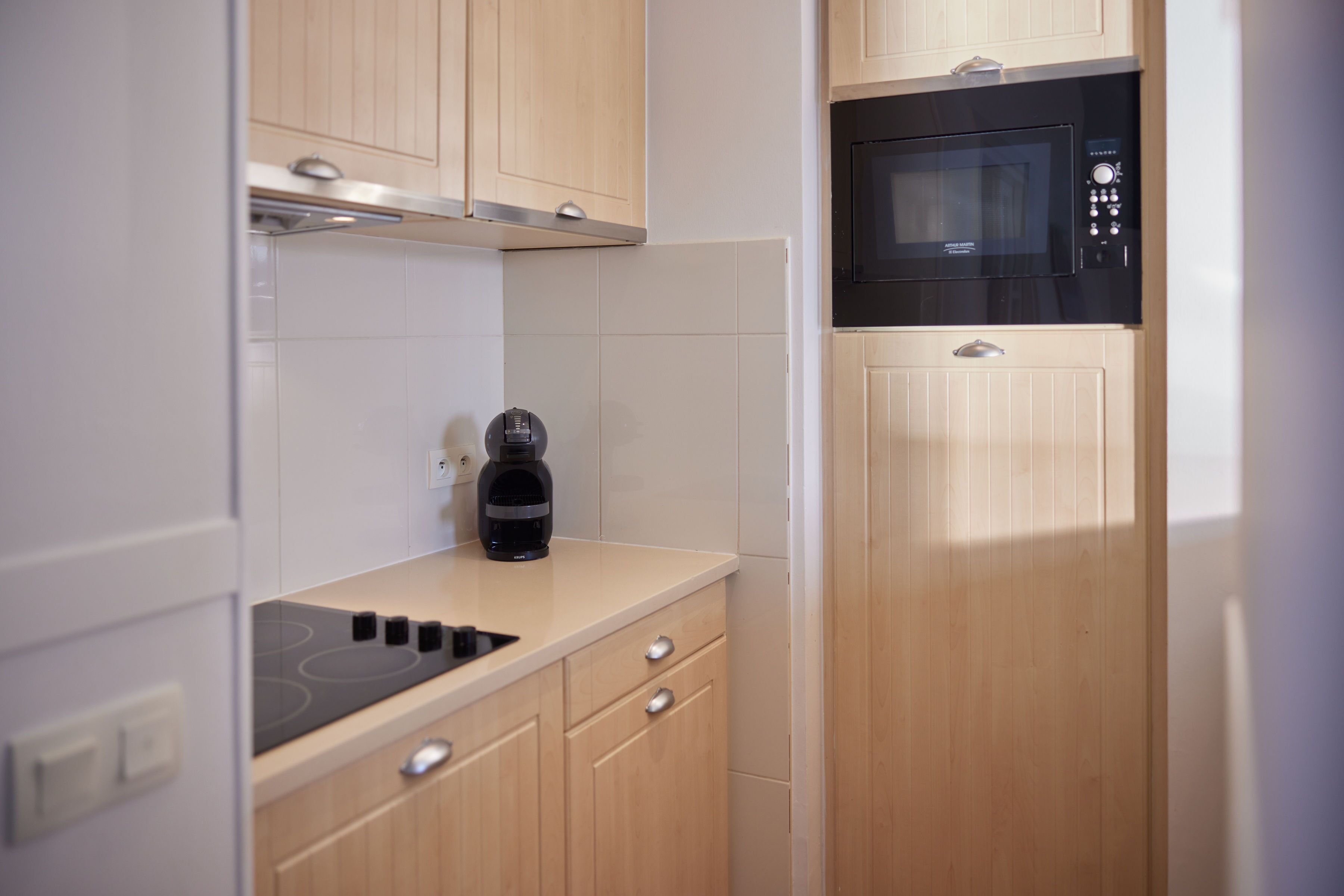 Une cuisine compacte avec des meubles de rangement en bois, un micro-ondes noir et une machine à café posée sur le plan de travail.