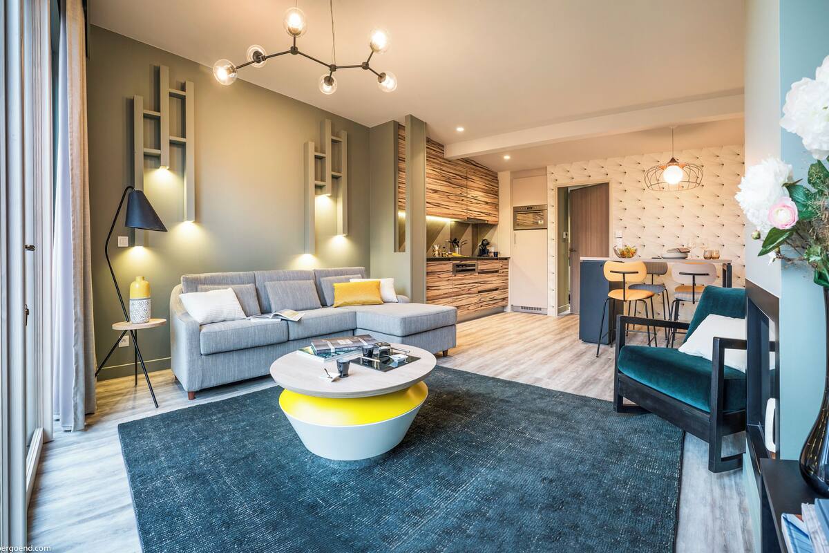 A modern living room with a grey sofa, a round coffee table, and a dining area with a table and chairs.