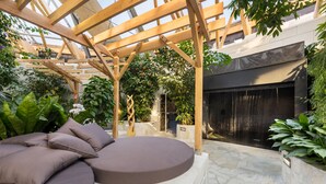 A covered outdoor seating area with a pergola, stone flooring, and lush greenery. - Center Parcs Les Trois Forêts (Fraquelfing)
