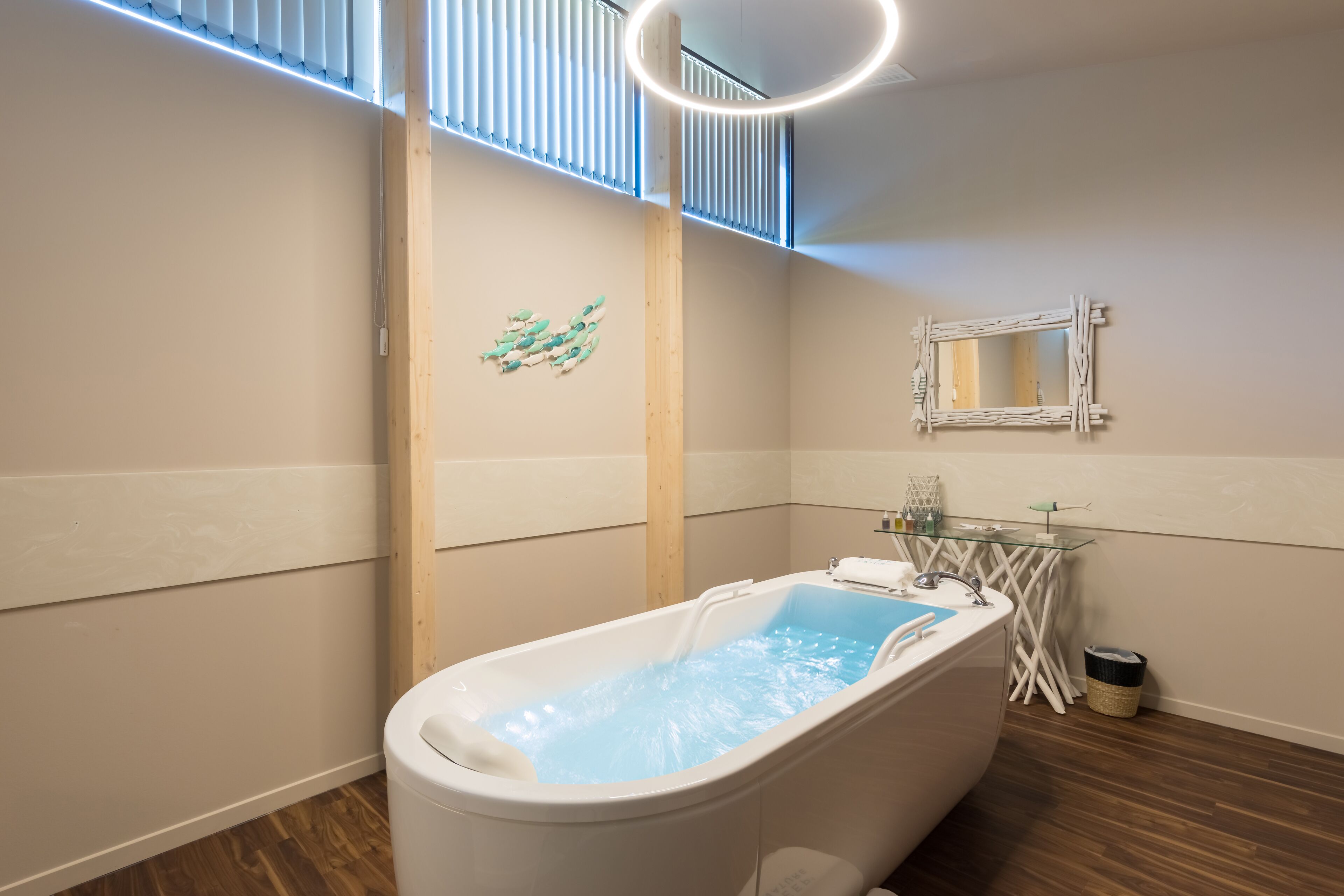 Un baño moderno con una bañera independiente, una mesita de vidrio con artículos de aseo y un espejo de pared original.