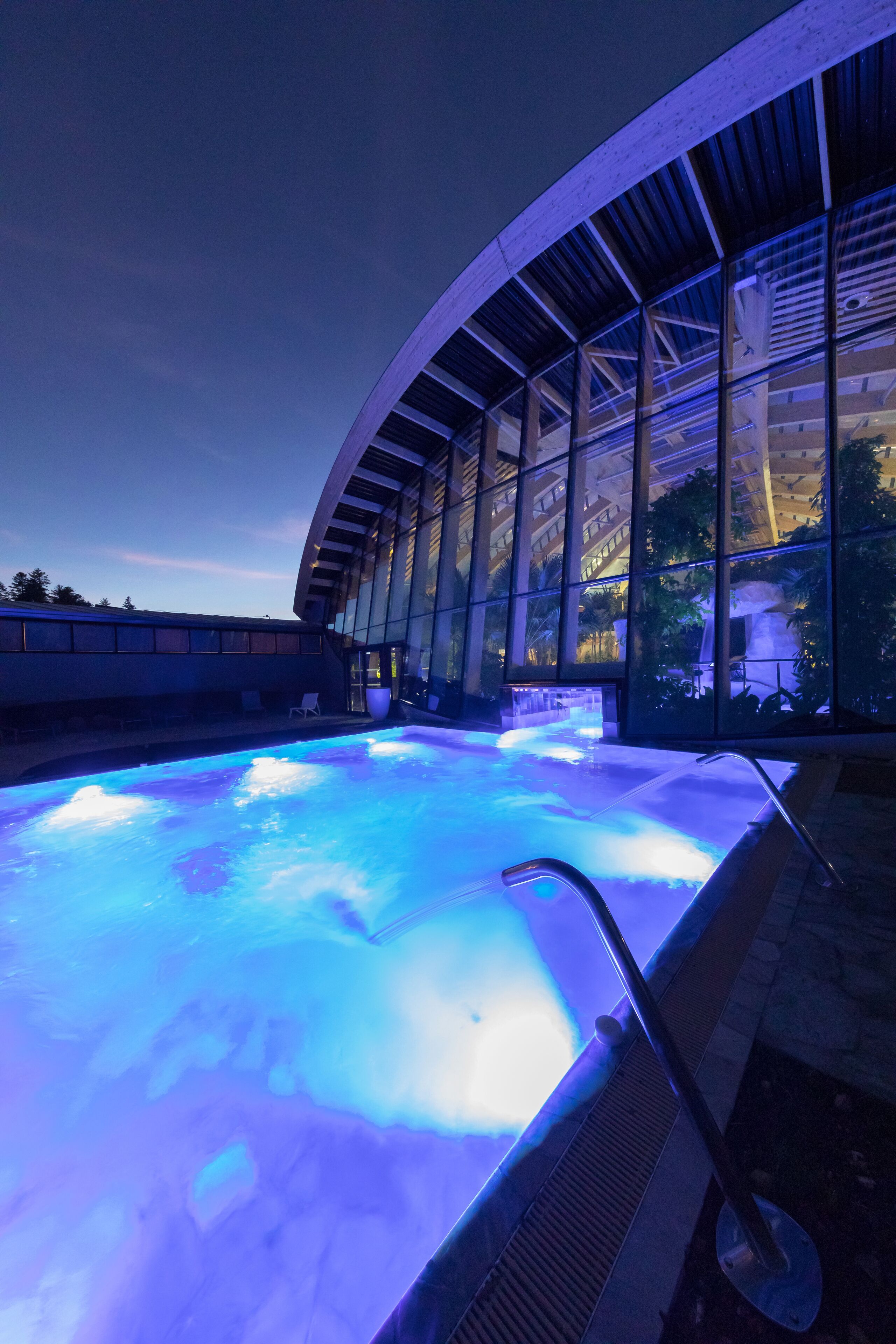 Ein großer, überdachter Pool mit gewölbter Glasscheibe, umgeben von moderner Architektur.