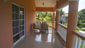 A balcony with a tiled floor, two wicker chairs, and a view of a garden with palm trees. - Beautiful 3 Bedroom ocean view villa in sosua (Sosúa)