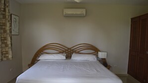A neatly made bed with a wooden headboard, a wall-mounted air conditioner, and a wooden wardrobe. - Beautiful 3 Bedroom ocean view villa in sosua (Sosúa)