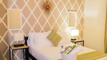 Cama bem arrumada com lençóis brancos, um cobertor verde e uma mesa de cabeceira com abajur e um pequeno bandeja de produtos de higiene pessoal.