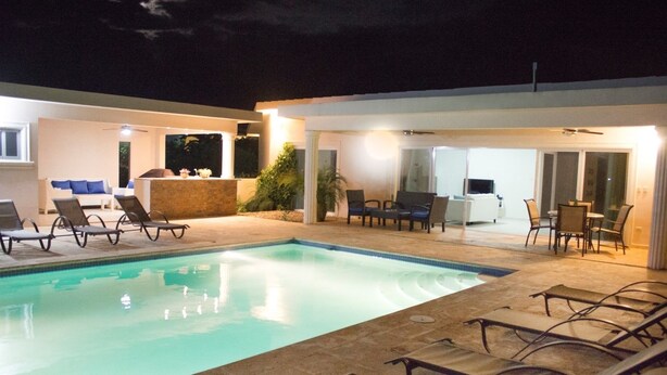 Piscina con sillones de descanso y un patio con mesas y sillas.