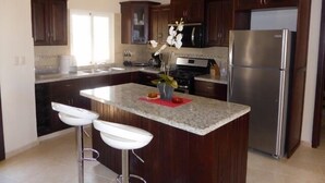 Una cocina moderna con armarios de madera oscura, un refrigerador de acero inoxidable, encimera de granito y taburetes de bar blancos.