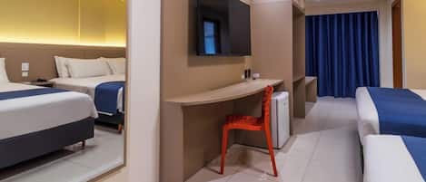 A hotel room with two beds, a desk, a chair, a TV, and a bathroom.