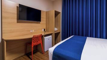 A hotel room with a bed, a desk with a chair, a television, and a small refrigerator.