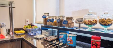 A kitchen counter with various food items, jars, and kitchen utensils.