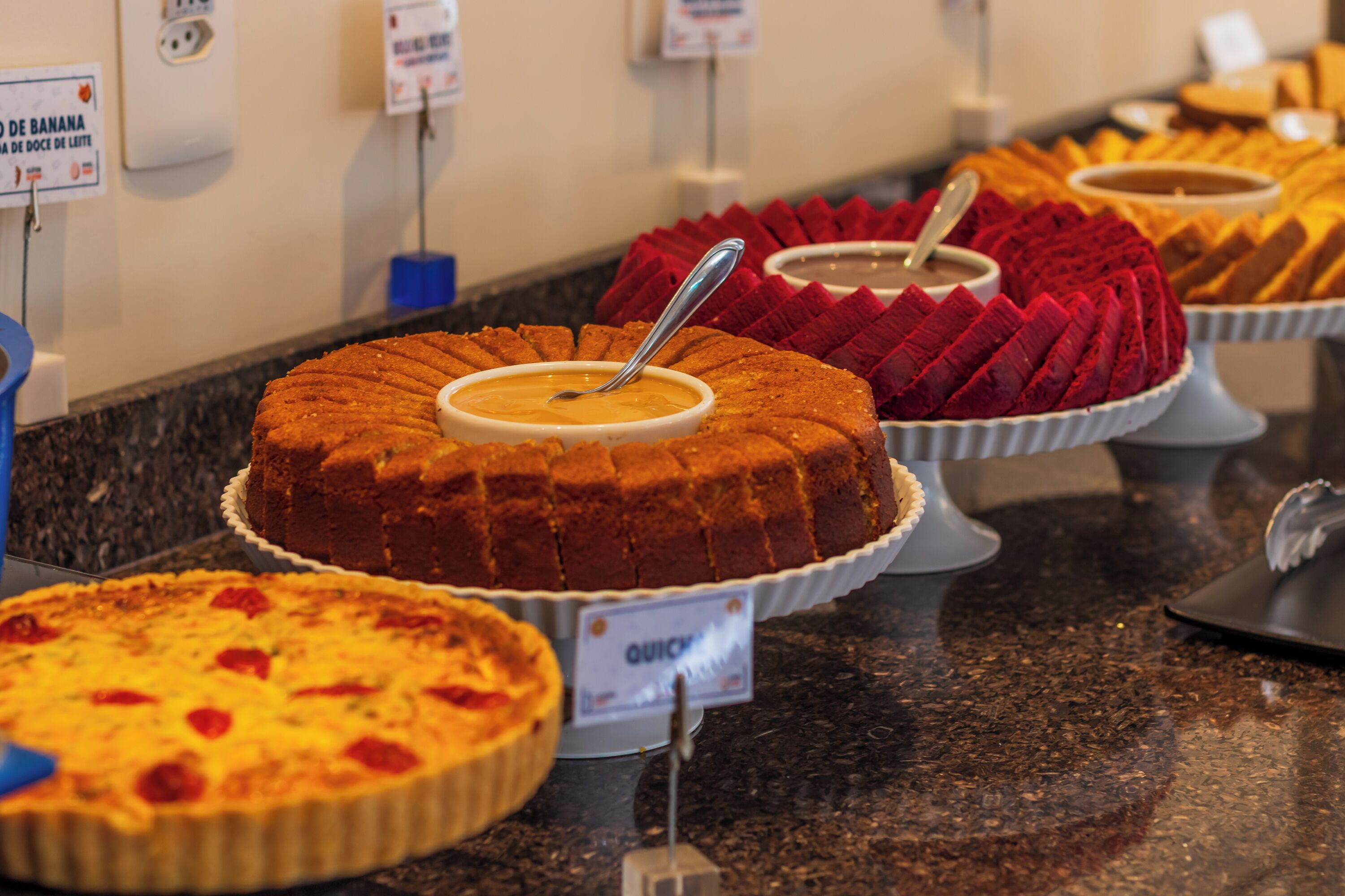 Een buffet met diverse desserts, waaronder een bundt cake, een red velvet cake en een taart met aardbeien.