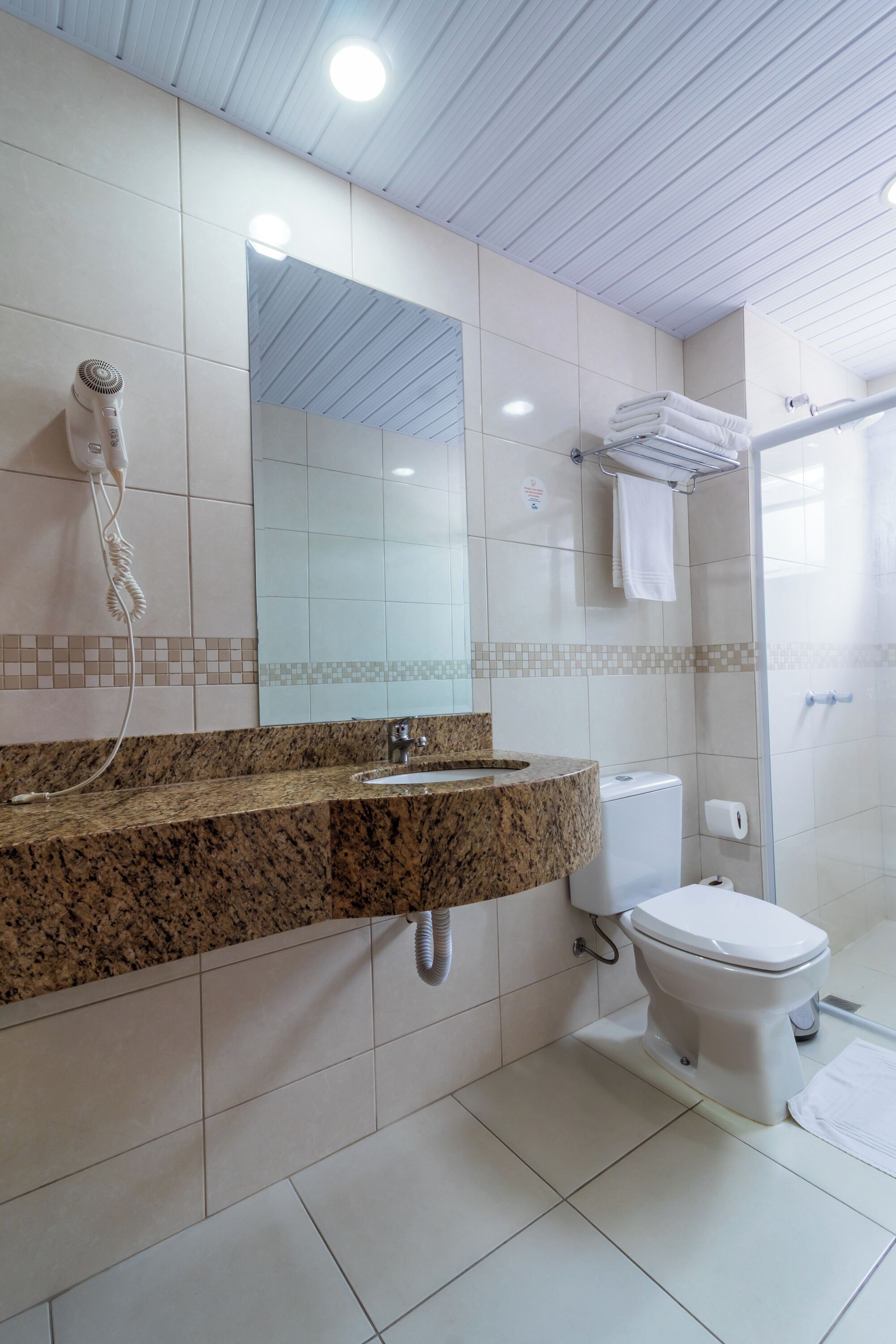 Un baño moderno con encimera de granito, inodoro blanco, ducha y un espejo grande.