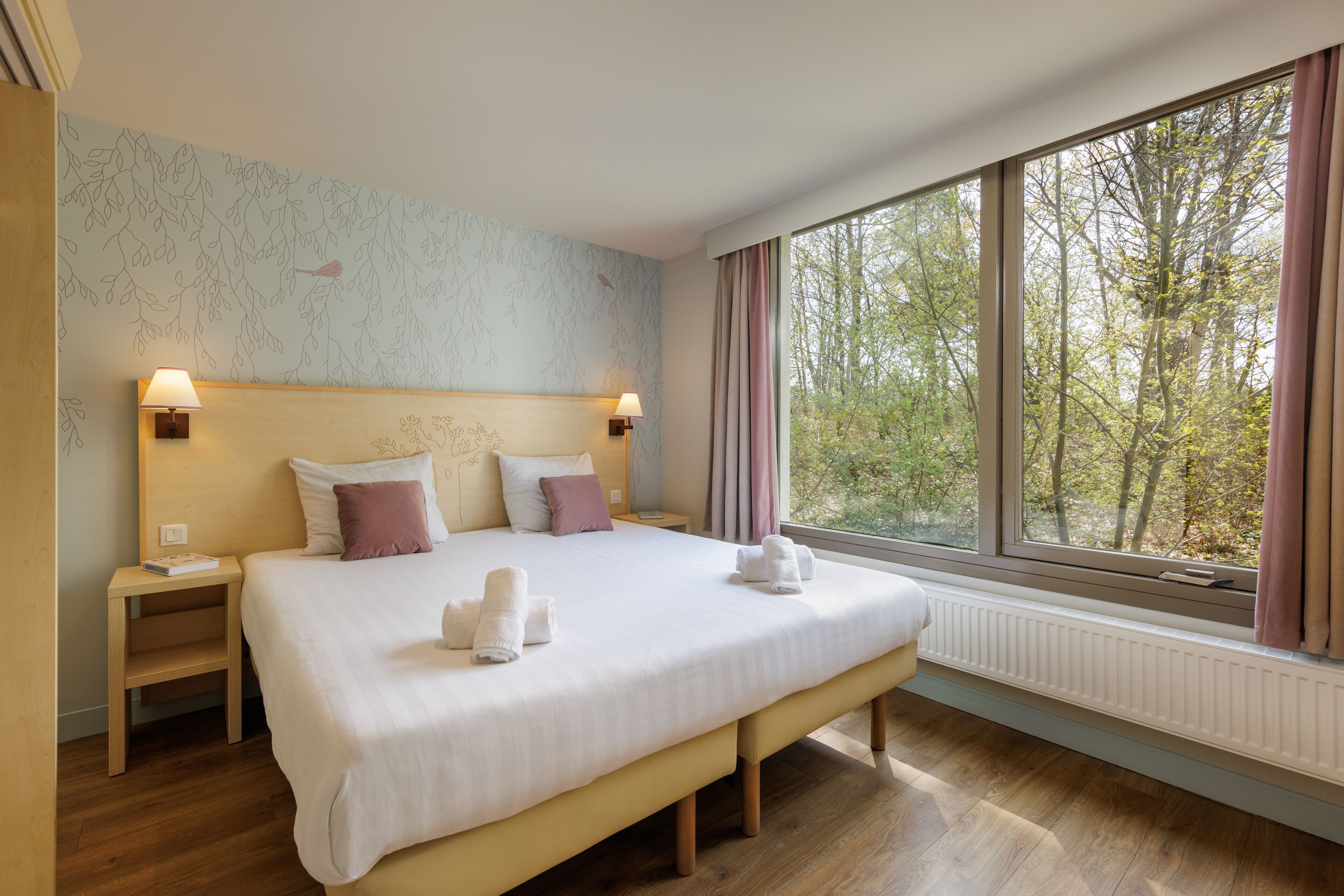 A spacious bedroom with a large bed, bedside tables, and a view of trees through a window.