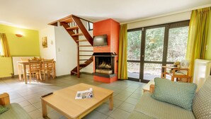 A living room with a fireplace, a sofa, a coffee table, a dining area with chairs, and a staircase. - Sunparks Kempense Meren (Mol)