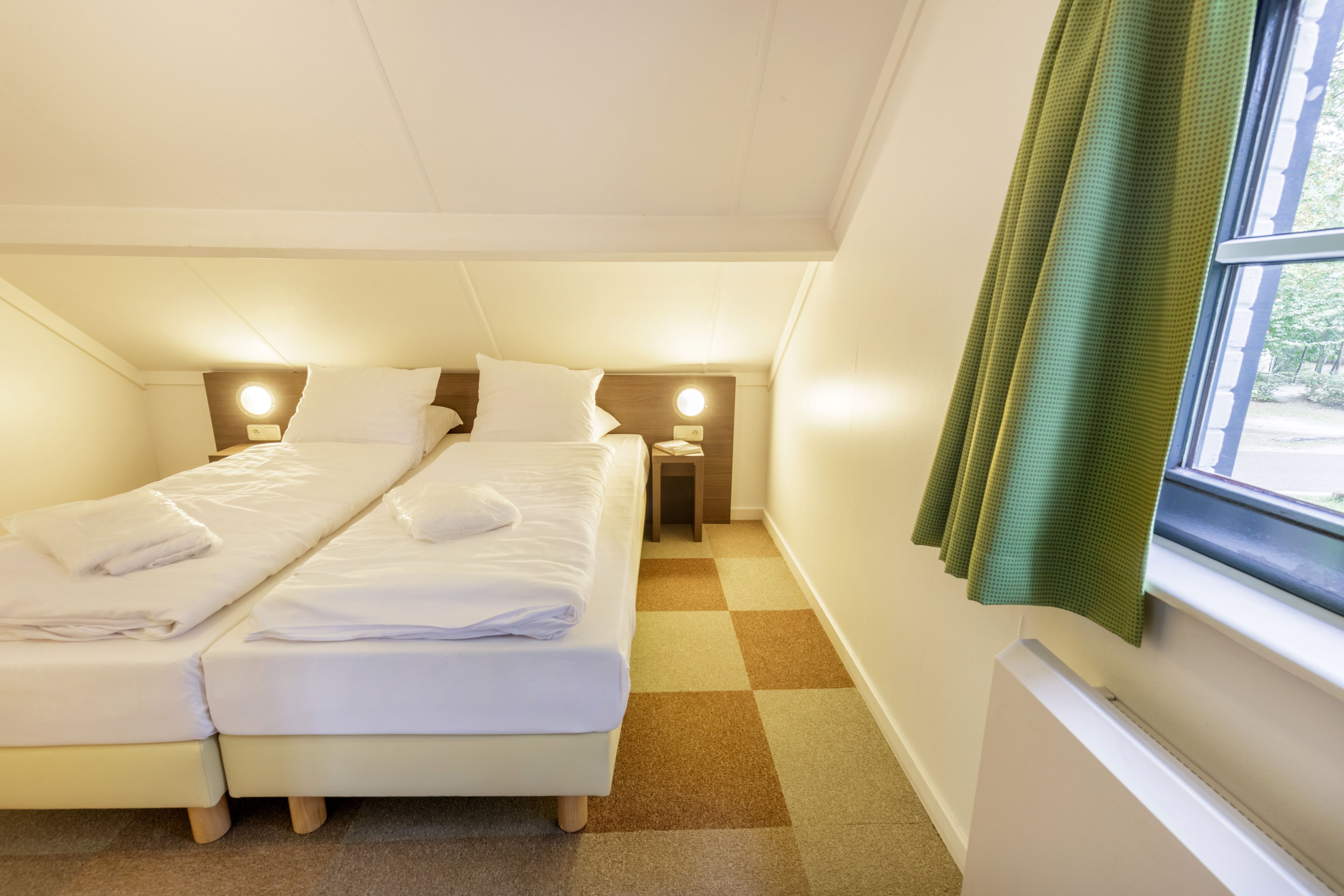 A twin room with two beds, a window with a green curtain, and a checkered floor.