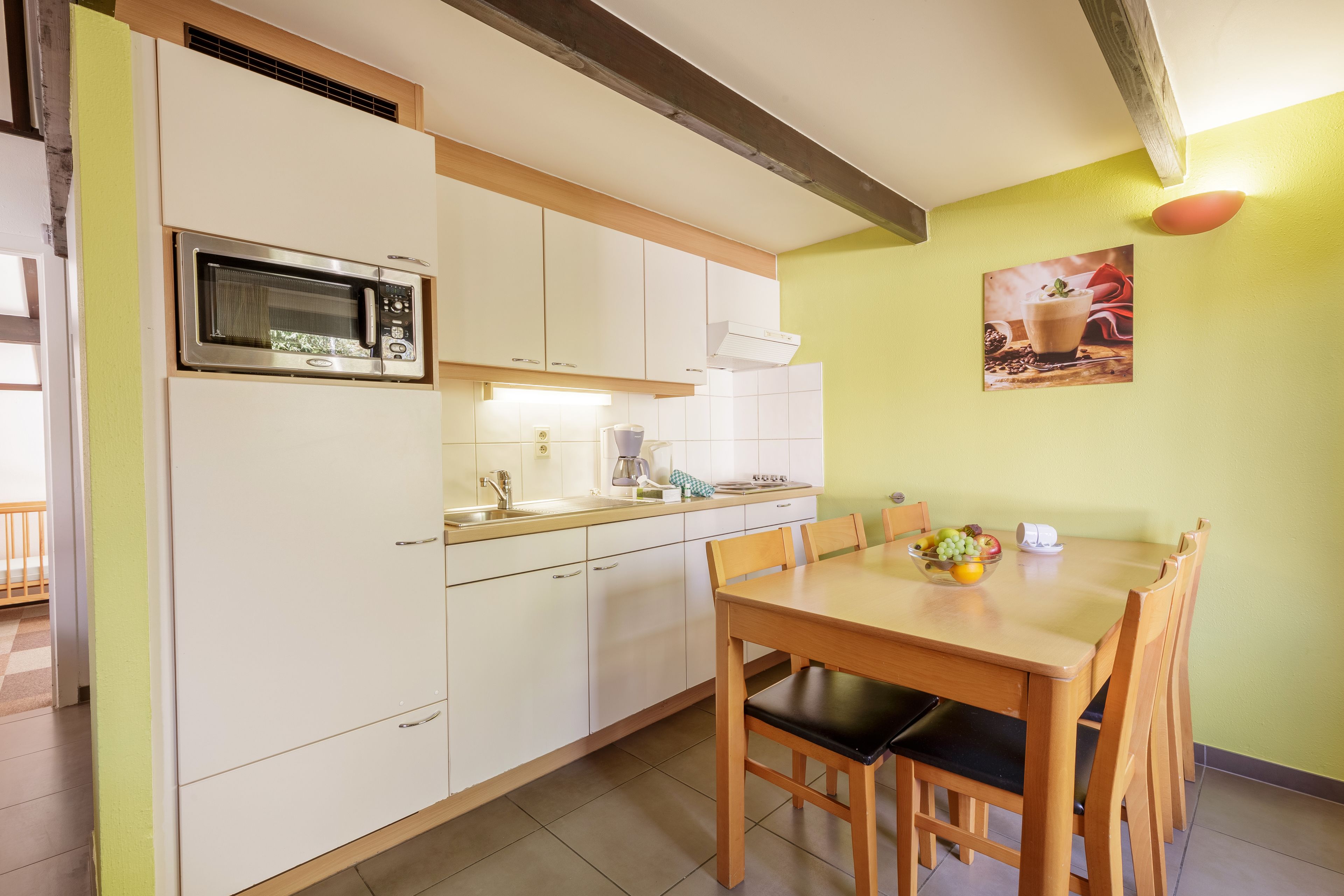 A compact kitchen with white cabinets, a microwave, a sink, and a dining table with chairs.