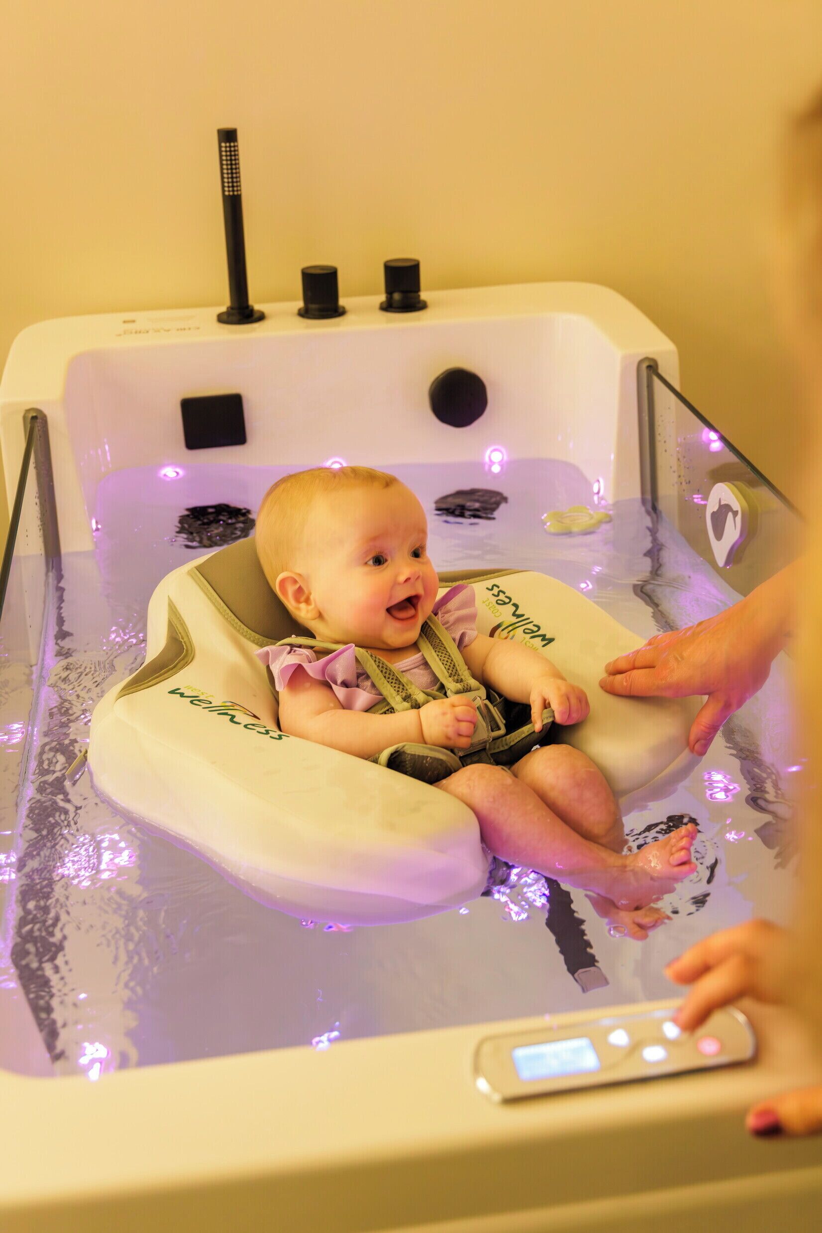 Um bebê em uma banheira com dispositivo de flutuação, uma torneira e um painel de controle.