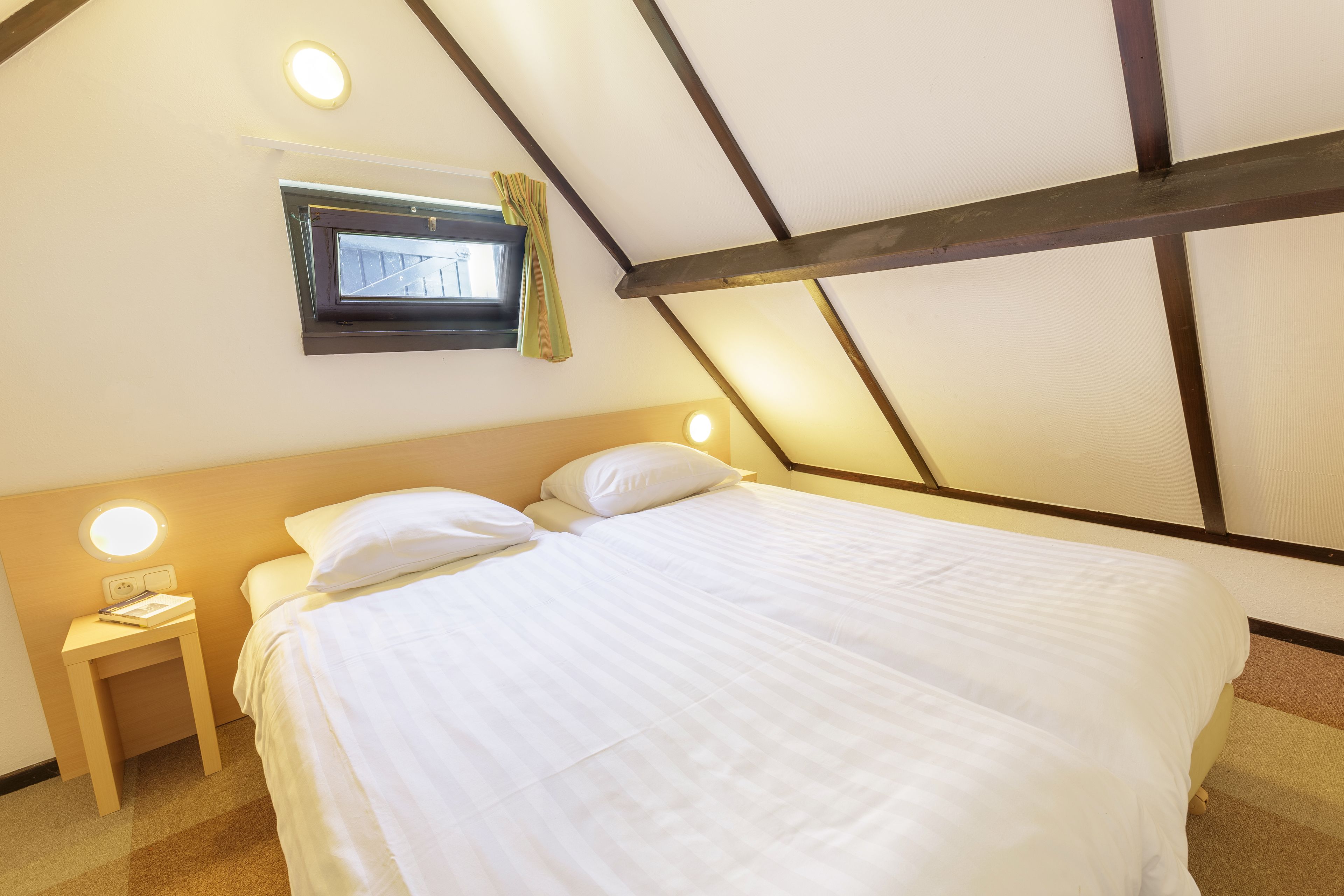 A bedroom with a bed, bedside tables, a window, and a ceiling with exposed beams.