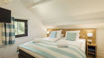 Een slaapkamer met een bed, een nachtkastje, een aan de muur bevestigde televisie en een raam met gordijnen.