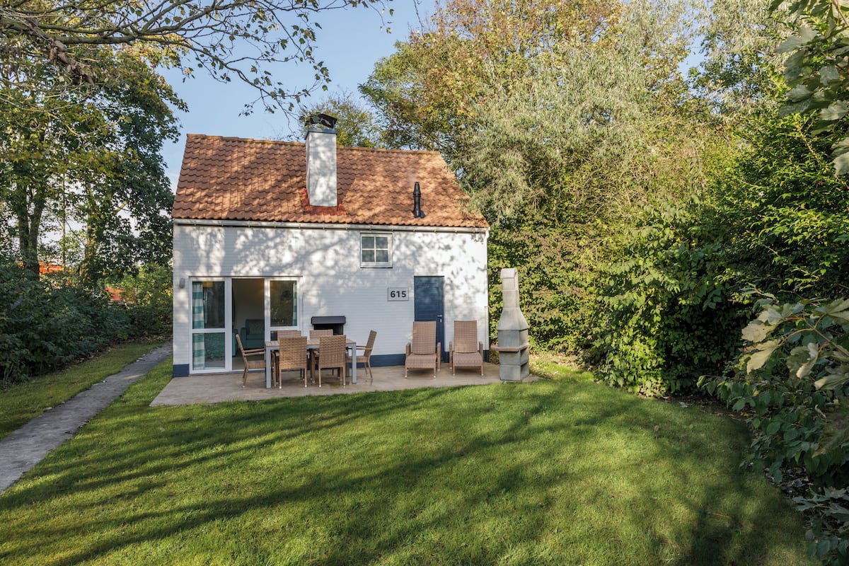 Une maison blanche avec un toit en tuiles, portant le numéro 615, dotée d’un patio avec des meubles d’extérieur et d’une cheminée.