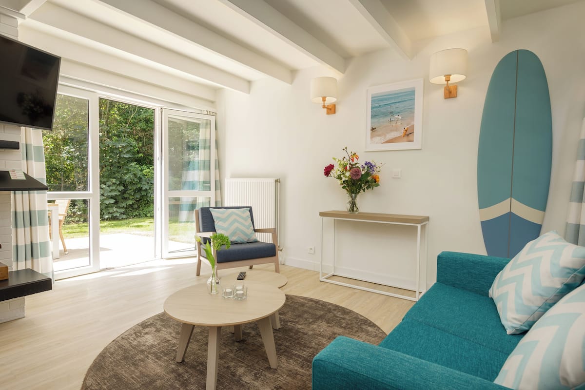 Un salon moderne avec un canapé de couleur turquoise, une table basse ronde et un téléviseur fixé au mur.
