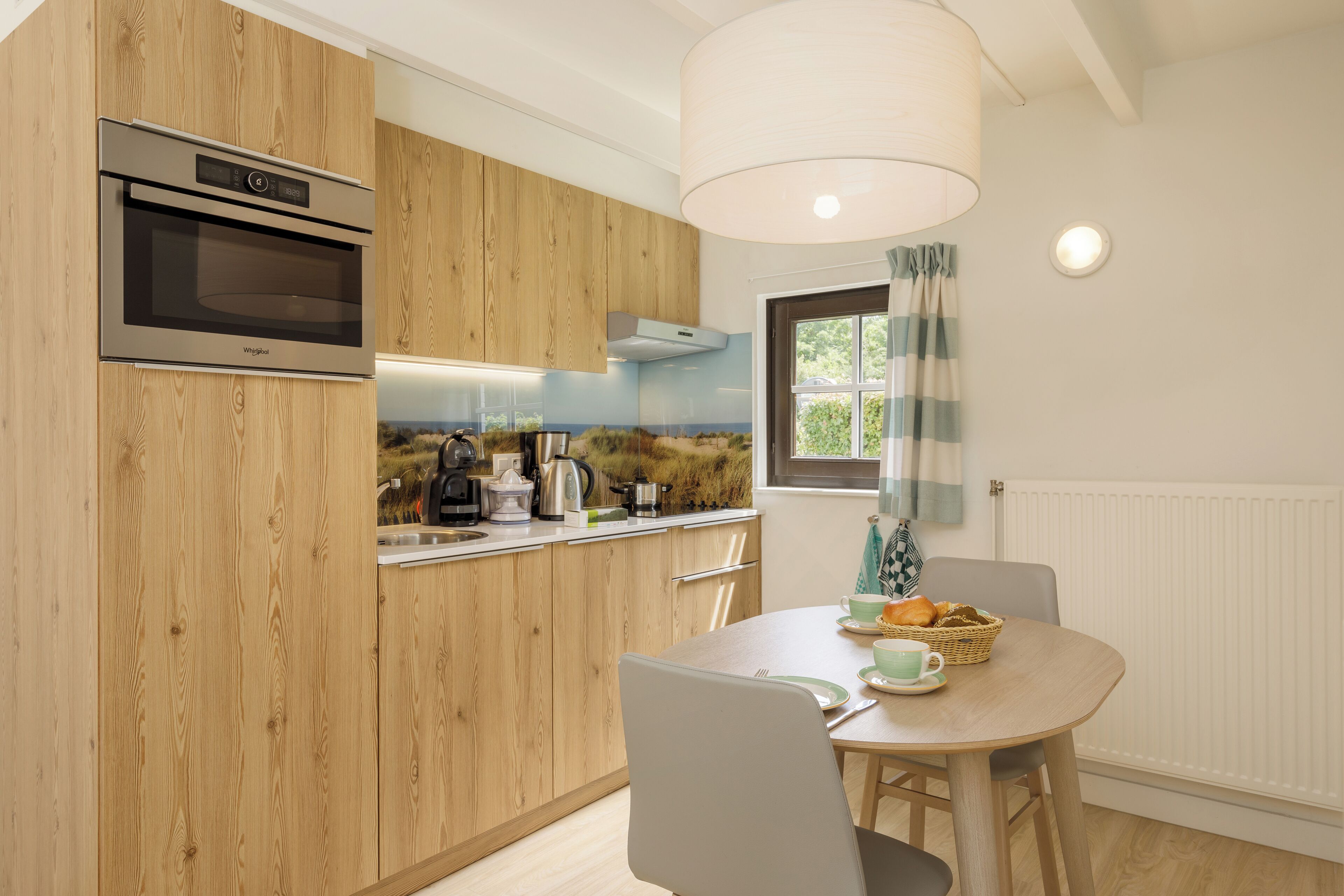A modern kitchen with wooden cabinets, a built-in oven, and a dining area with a table and chairs.