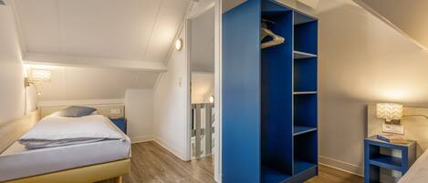 A bedroom with a bed, a blue wardrobe, a nightstand, and a staircase leading to another room.