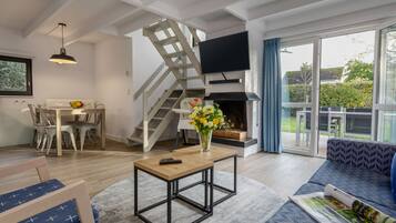 Un salon moderne avec une table basse en bois, un canapé, un téléviseur fixé au mur et un escalier menant à un niveau supérieur.