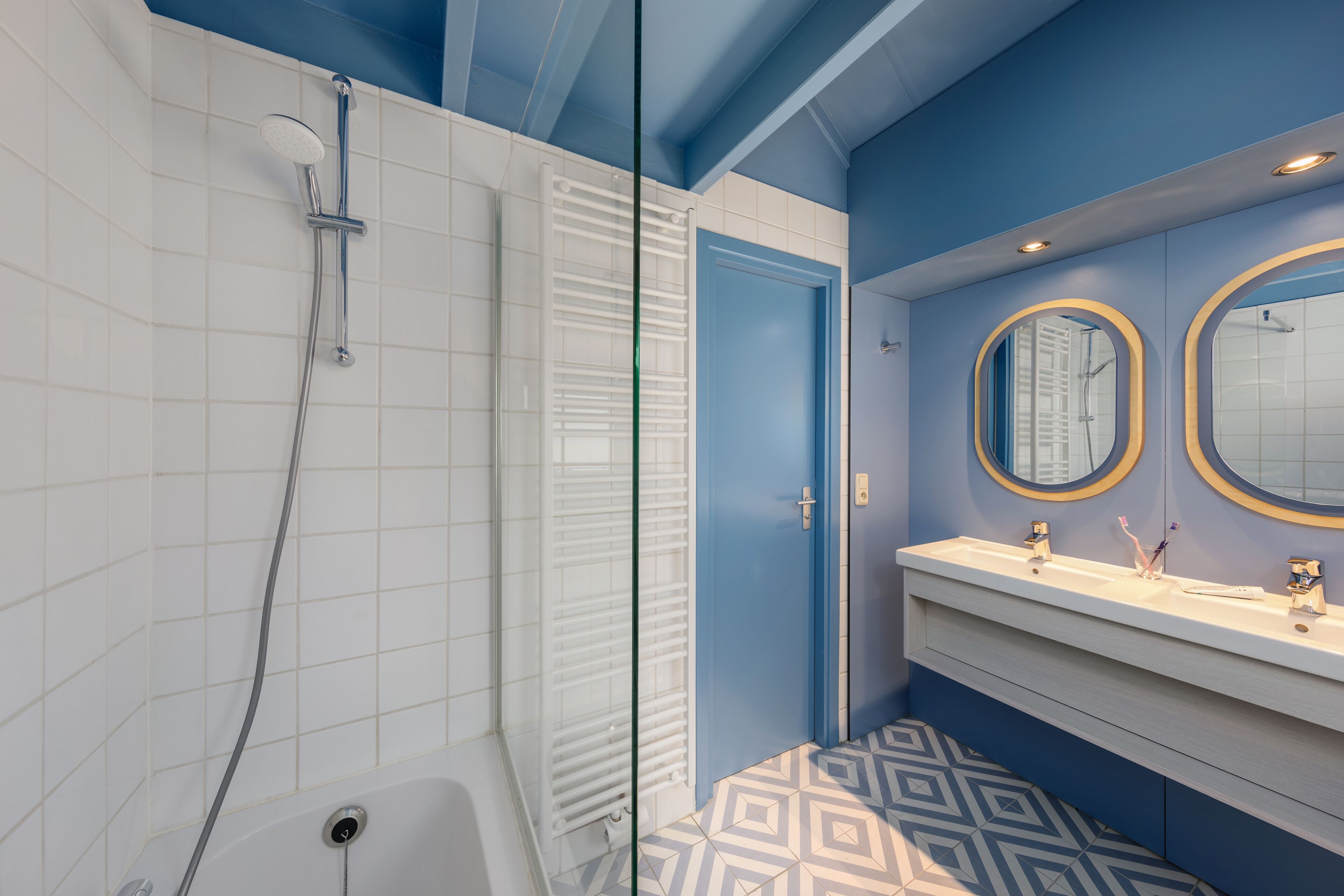 A bathroom with a shower, a sink with two mirrors, and a patterned floor.