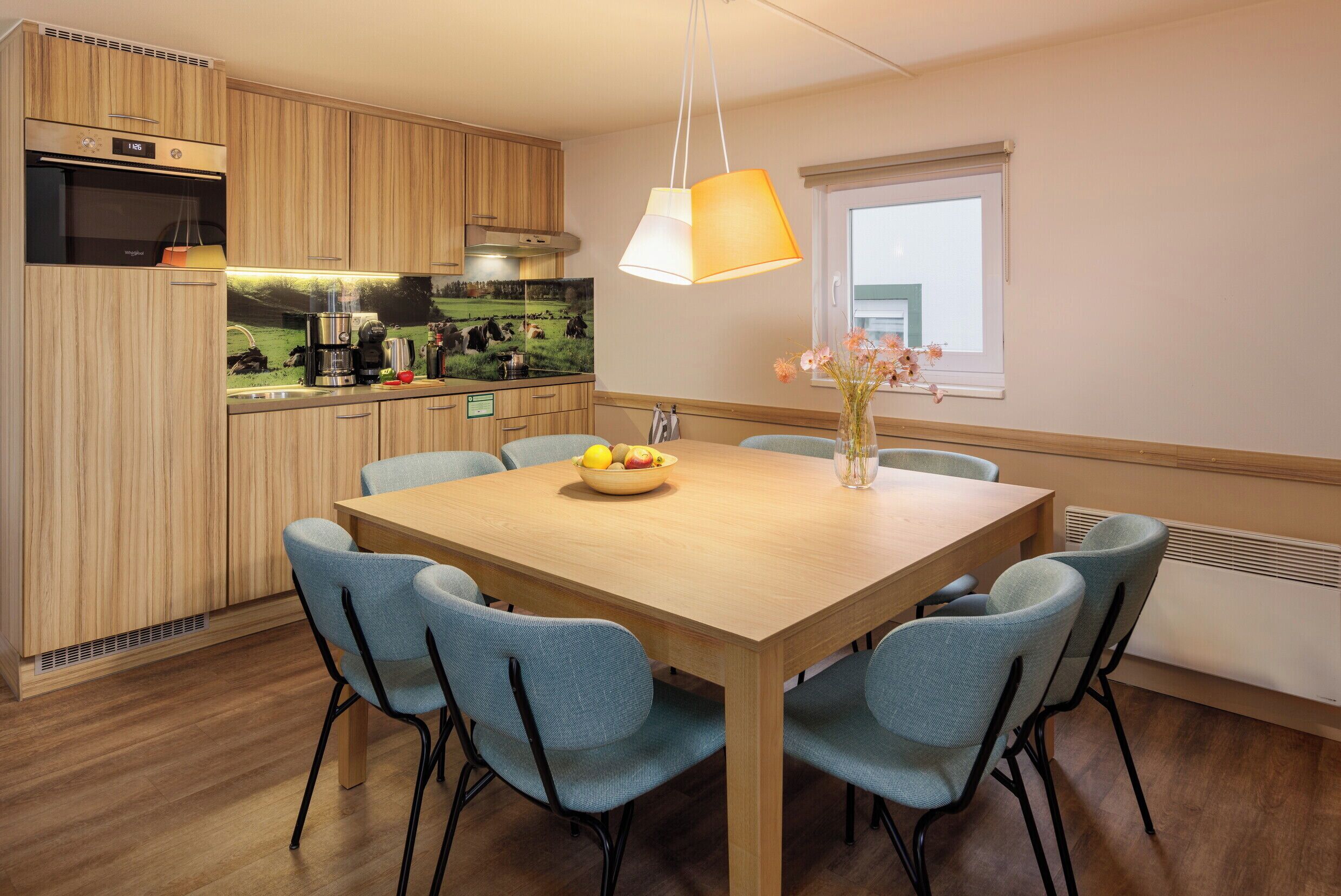 Une cuisine moderne avec des meubles en bois, un four encastré et un coin repas comprenant une table en bois et des chaises bleues.