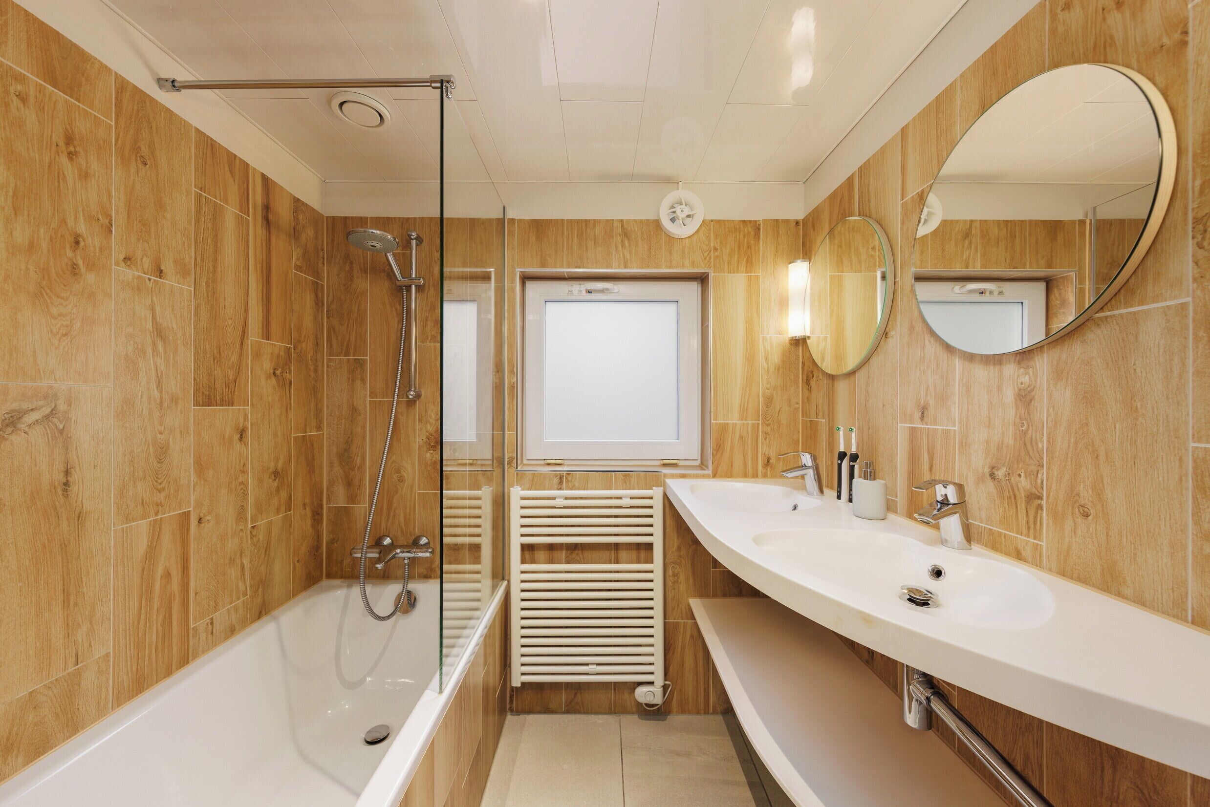 Een moderne badkamer met een douche met glazen wand, twee wasbakken en een spiegel.