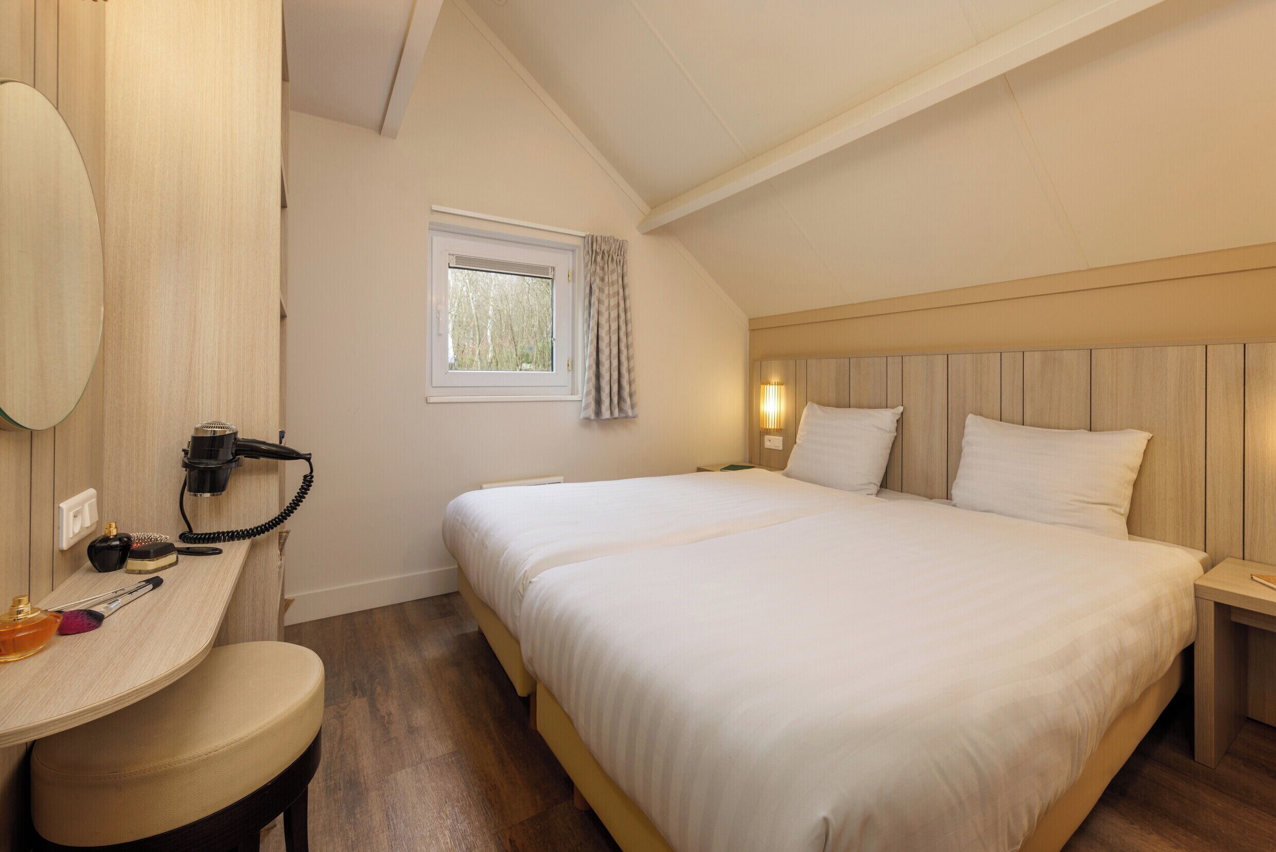 A bedroom with a bed, a desk with a hairdryer, and a window with curtains.