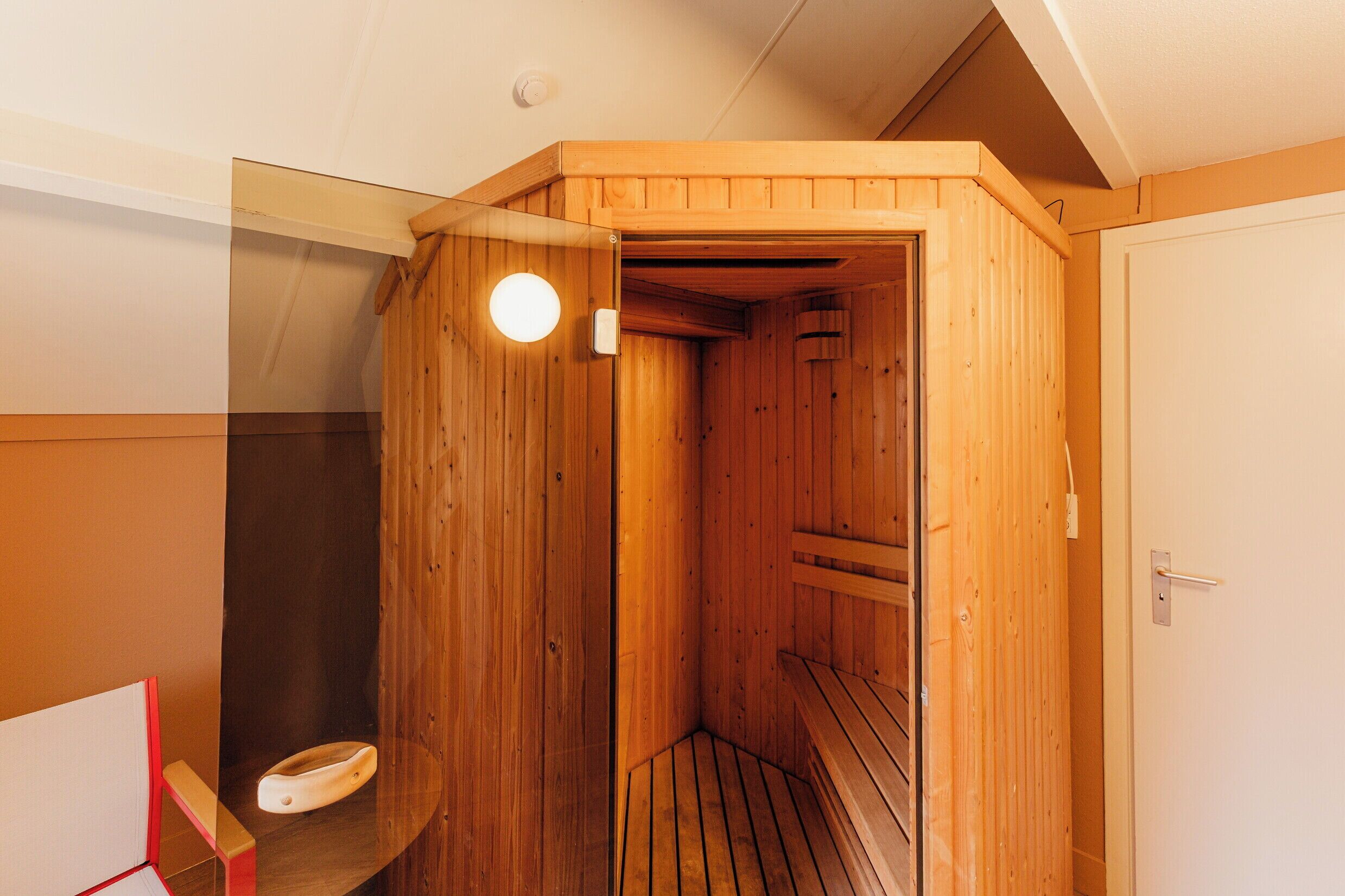 Una sauna de madera con un banco, una puerta y una lámpara.