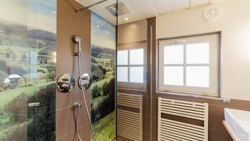 A bathroom with a glass shower enclosure, a window, a radiator, and a bathtub.