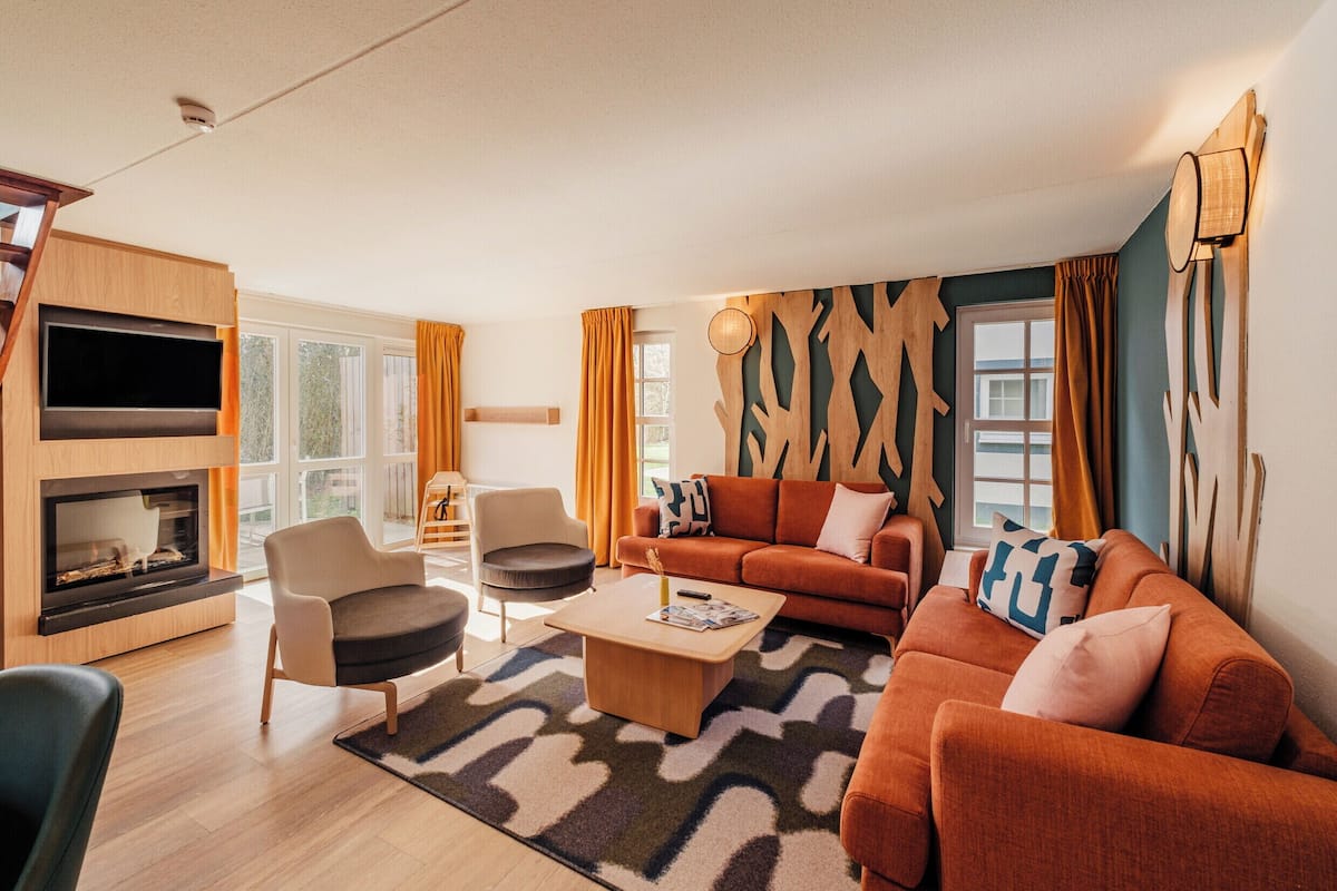 Un salon moderne comprenant un canapé, des fauteuils, une table basse, une cheminée et un grand téléviseur.