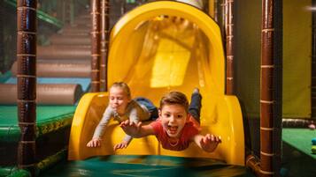 Des enfants glissent sur un toboggan jaune dans un espace de jeux intérieur.