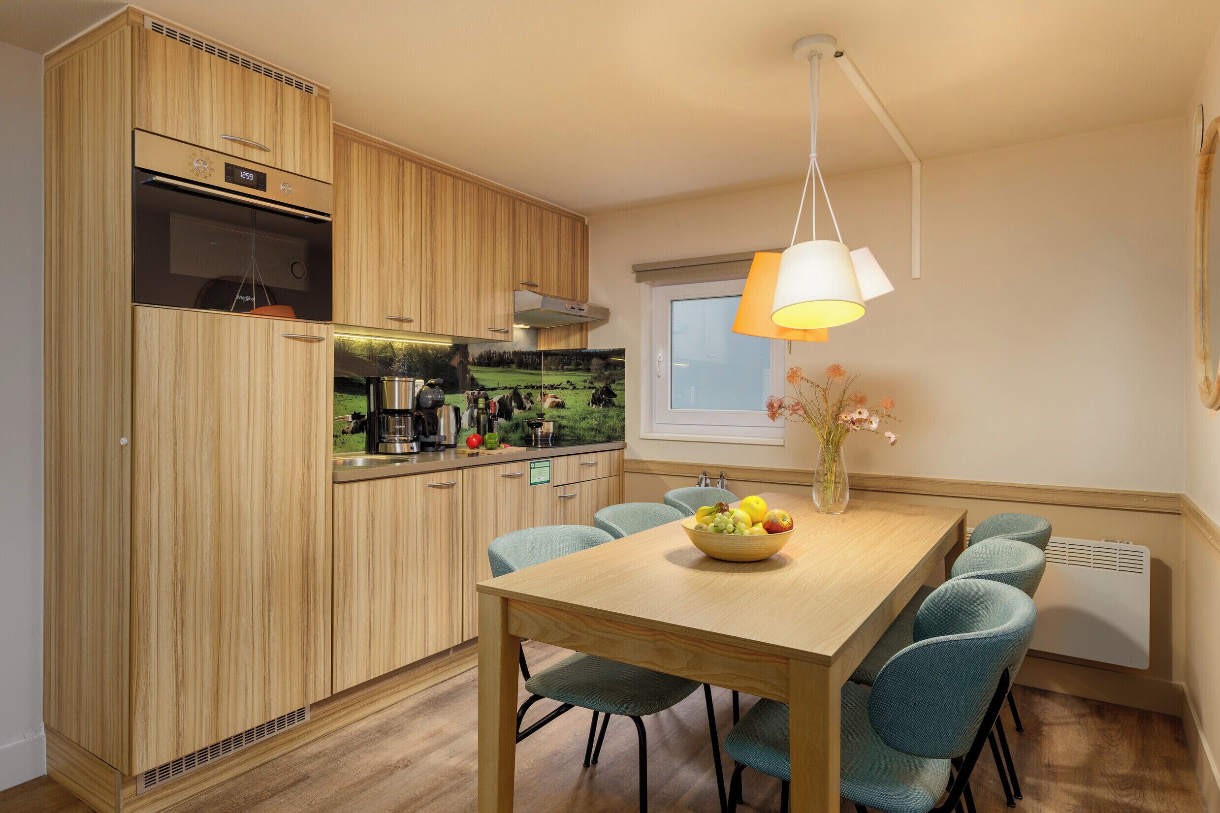 Een moderne keuken met houten kasten, een inbouwoven en een eethoek met een tafel en stoelen.