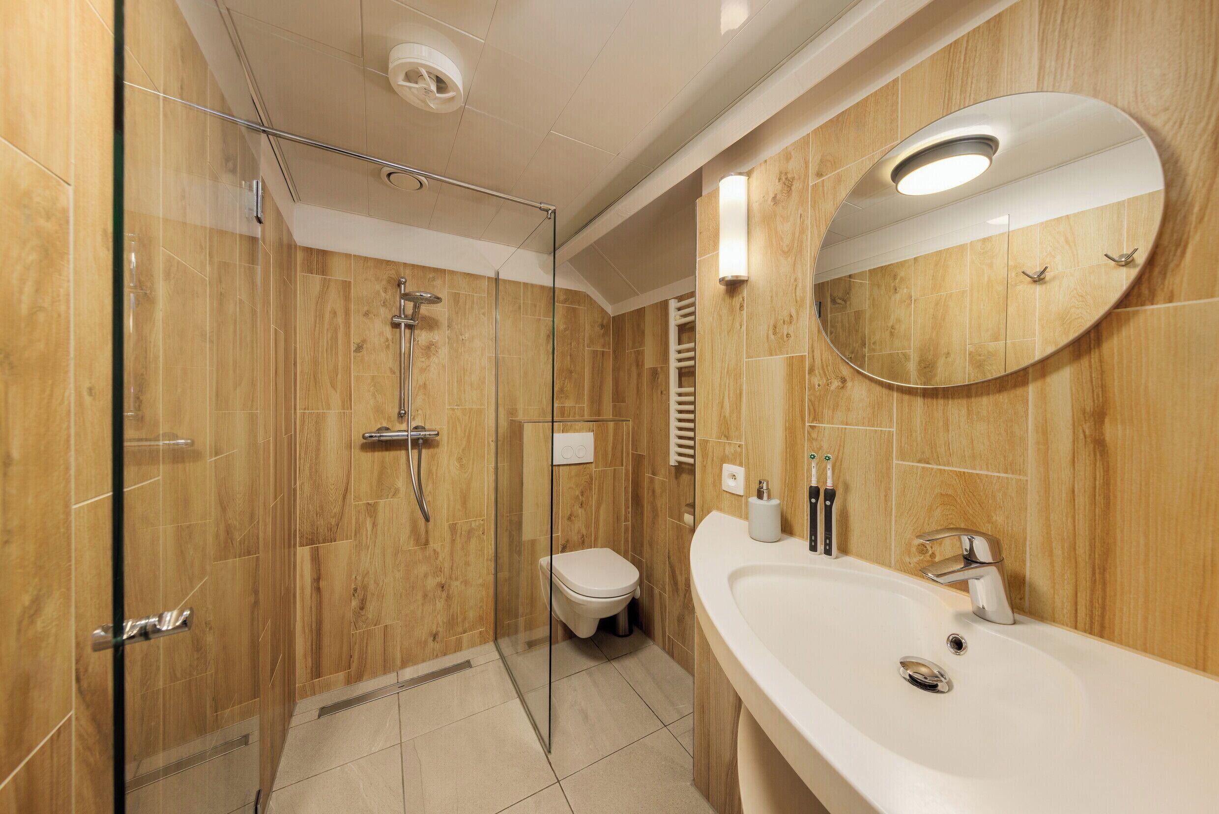 A modern bathroom with a glass-enclosed shower, a white sink, and a large mirror.