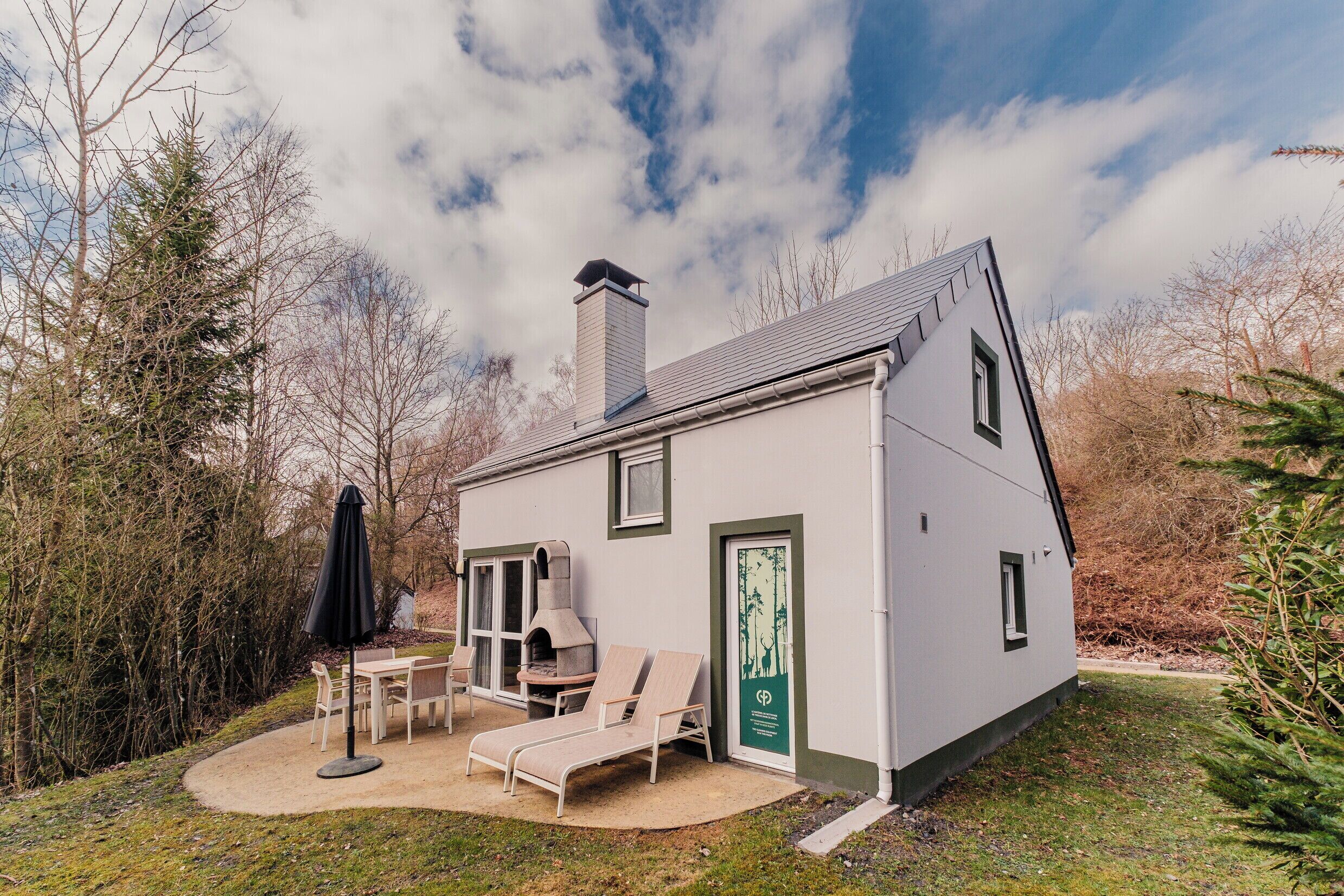 A small house with a chimney, a patio with a table and chairs, and a door with a forest decal.