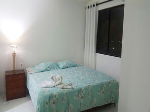 Un dormitorio con cama, mesita de noche, lámpara y ventana con cortinas.
