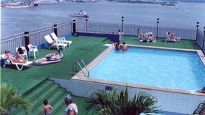 Un espace piscine avec vue sur la mer, entouré d’une clôture, et comprenant des marches menant à la piscine.