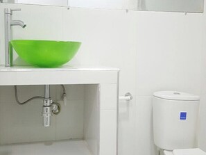 Un baño con un lavamanos blanco, un cuenco verde, un inodoro y un letrero azul en la pared.