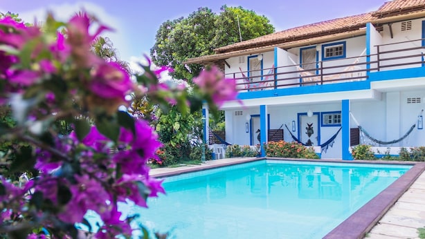 A swimming pool with a blue and white building in the background. - Pousada Pedra D'Água (Tibau do Sul)