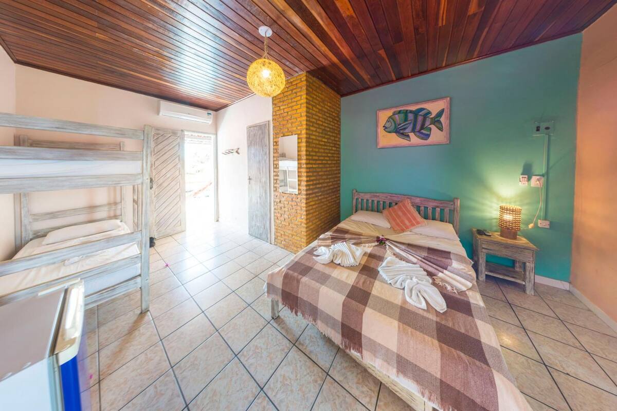 A room with a bed, a wooden bench, a brick wall, and a fish painting.