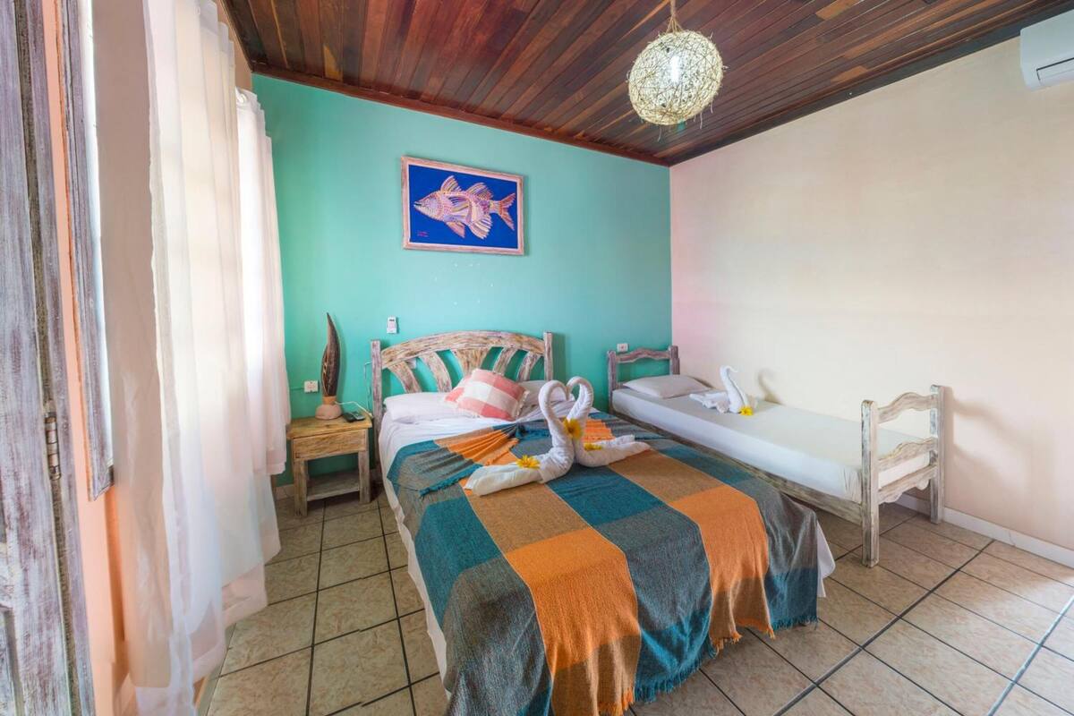 A room with a bed, a small table, a bench, and a wall-mounted picture.