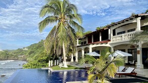 A poolside view of a resort with a clear view of the ocean, palm trees, and a two-story building with a balcony.
