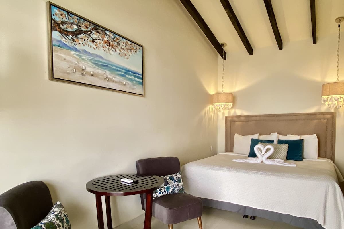 A hotel room with a bed, a chair, a small table, and a painting on the wall.