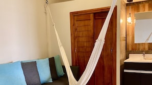 A room with a hammock, a wooden door, a sofa with cushions, and a bathroom with a sink and mirror.