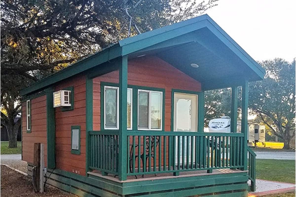 A small, single-story cabin with a green porch and a red exterior.