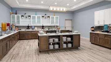 Uma cozinha moderna com armários de madeira, uma ilha central com pratos empilhados e diversos eletrodomésticos.